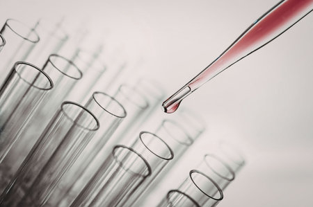 A dropper is releasing a red liquid into one of several test tubes arranged in a row.