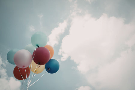 A bunch of colorful balloons floating in the sky with white clouds.