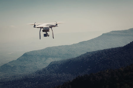 A drone flies over a rugged mountain range with a clear sky in the background.