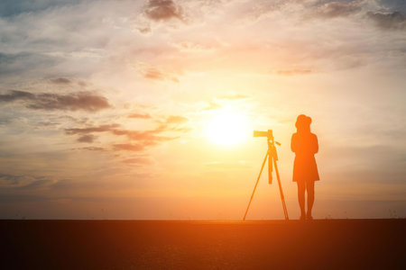A photographer stands on a field, capturing the sunset with a camera on a tripod.