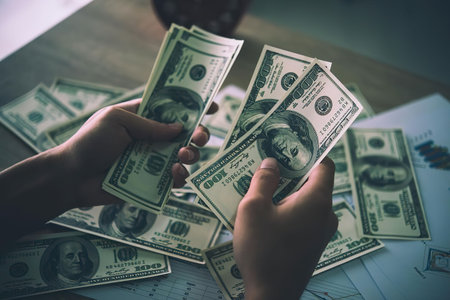 A person holding dollar bills in their hands with more bills scattered on a table.