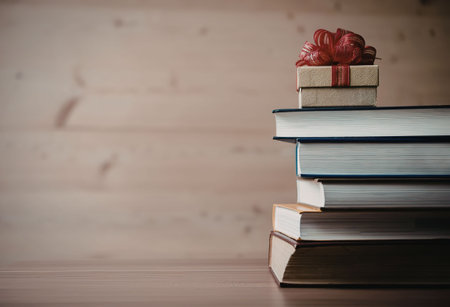 A stack of books with a gift box on top, wrapped in red ribbon, on a wooden table against a wooden...