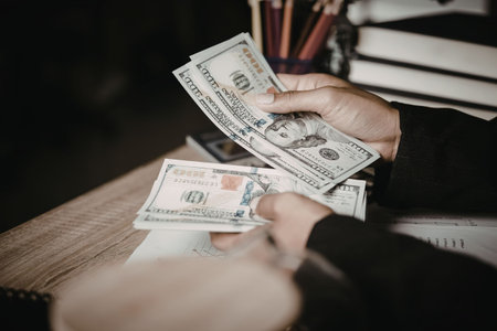 A person is handling dollar bills on a desk, possibly counting or organizing money.