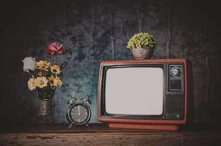 A retro television with a blank screen sits on a table next to a vase of flowers and an alarm clock.
