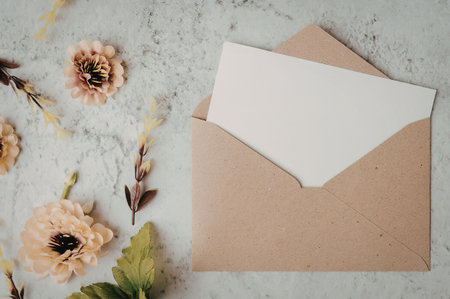 A brown envelope with a white insert on a marble surface with yellow flowers
