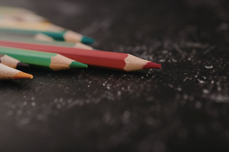 A close-up view of colored pencils on a black surface, with a red pencil in focus.