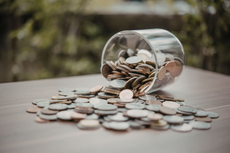 A glass jar lying on its side with coins spilling out onto a wooden surface.