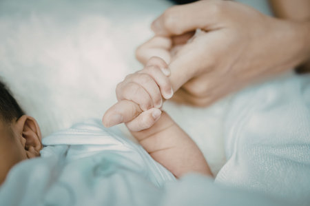 A close-up photo of a newborn baby holding an adult's finger, conveying a sense of love, care, and...