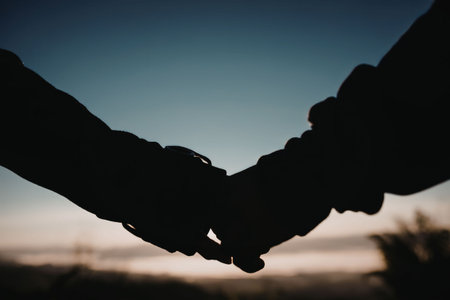 A silhouette of two hands clasped together against a sunset background