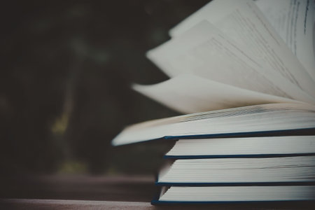 A stack of books with one book open on top, displaying its pages.