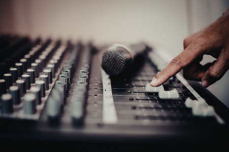 A hand adjusting the levels on a professional audio mixing console with a microphone on it.