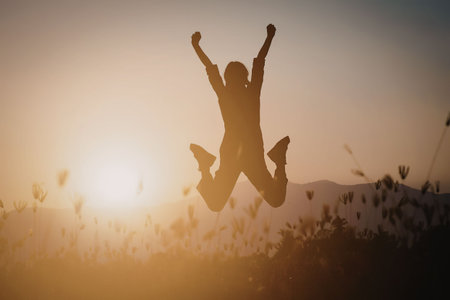 A person jumping in the air with arms raised at sunset