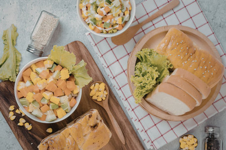 An arrangement of food items including bread, vegetables, and corn on a table with a wooden cutting...
