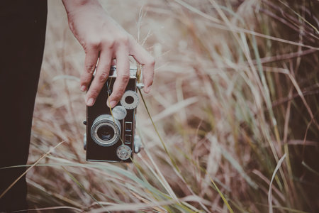 A hand holding an old camera in a field of tall grass.