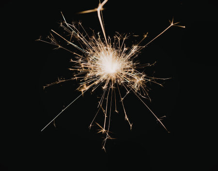 A sparkler burns brightly against a dark background, producing a burst of sparks.
