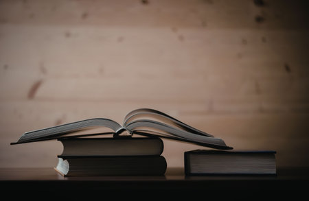 A stack of books on a wooden table with one book open and the others closed.