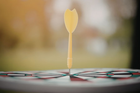 A close-up of a dartboard with a single yellow dart hitting the center bullseye, set against a...