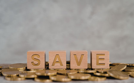 The image depicts a creative representation of saving money, with wooden blocks spelling out 'SAVE' placed on top of a pile of gold coins.の写真素材