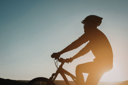 A silhouette of a man riding a bicycle against a vibrant sunset background.