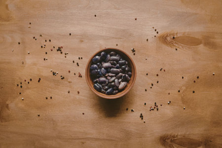 A small terracotta bowl filled with beans sits on a wooden table, surrounded by scattered beans.
