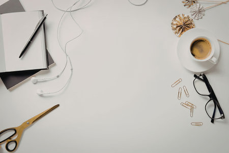 A flat lay of a cup of coffee, glasses, scissors, notebooks, and paper clips on a white desk.