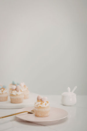 a cupcake with white frosting and pink and blue marshmallow on top sits on a pink plate, with more...