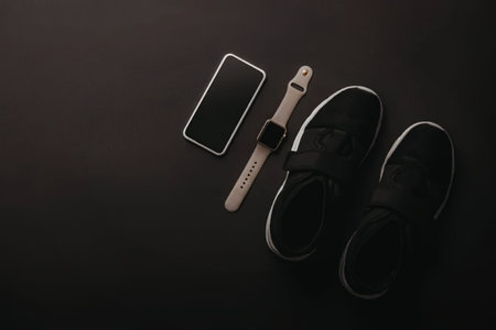 A pair of black shoes, a smartphone and a watch on a dark surface