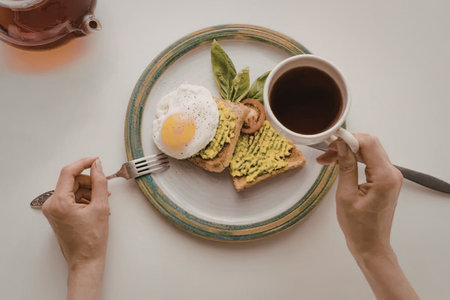 A person is having breakfast with a cup of coffee, toast with avocado and egg