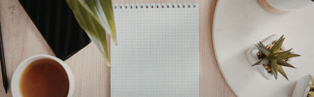 A serene workspace setup featuring a spiral notebook, a cup of tea, and potted plants on a wooden...