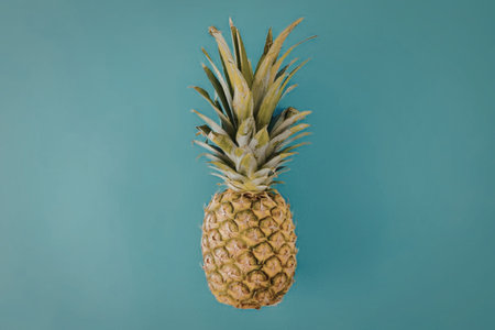 A vibrant and healthy pineapple centered on a plain blue background, emphasizing its yellow and...