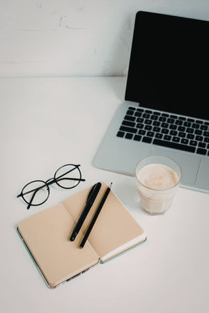 A minimalistic workspace setup with a laptop, notebook, pens, glasses, and a cup of coffee.