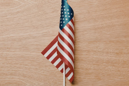 A small American flag on a white pole against a light brown wooden background