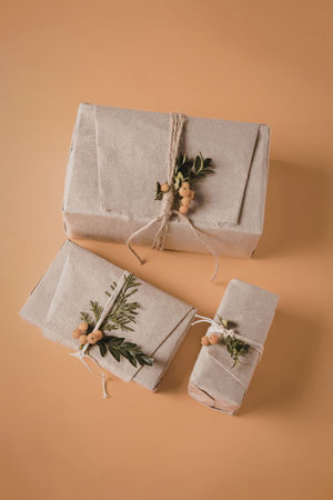 Three elegantly wrapped gifts with natural elements like twine, leaves, and berries on an orange...