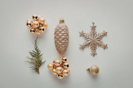 The image features a collection of Christmas ornaments and decorations arranged on a white surface. The items include two gold and orange flower-shaped ornaments, a pinecone, a gold snowflake, a small gold ball, and a sprig of pine.の写真素材