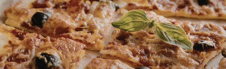 A close-up view of a pizza with basil leaves and olives on top, showcasing its savory and appetizing...