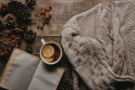 A warm and cozy winter still life with a cup of tea, a book, and a sweater on a wooden table with...