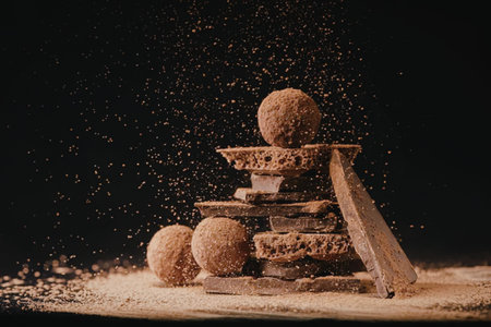 A stack of chocolate truffles with cinnamon sticks and powder scattered around on a dark background