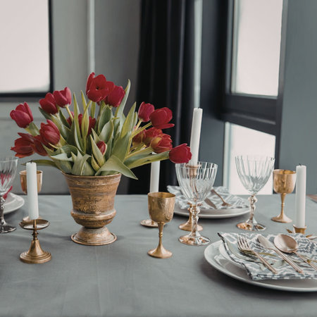 A beautifully set dinner table with a vase of red tulips, candles, and fine china, suggesting a...