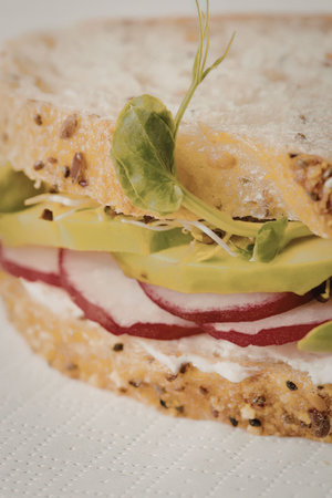 A close-up of a sandwich with radish, pepper, and greens on a white surface.
