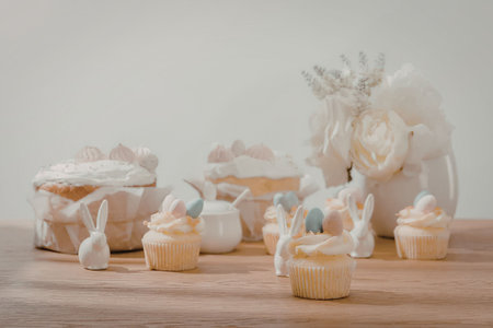 A wooden table with Easter themed cupcakes and bunny shaped treats, decorated with pastel colors and...