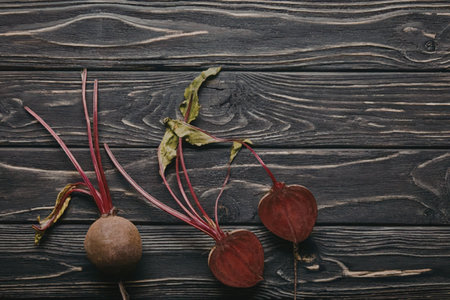 Three fresh beets with green leaves on a dark wooden surface