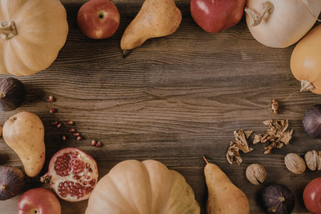 A variety of fresh fruits and vegetables arranged on a wooden table, including pears, apples,...