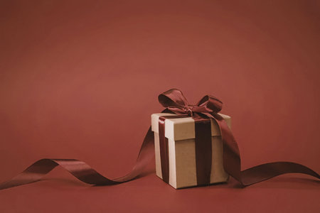 A gift box wrapped with a red ribbon on a matching red background, symbolizing a present or a...
