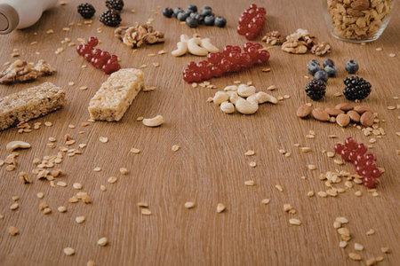 A wooden table with granola, fresh berries, and nuts scattered across it.