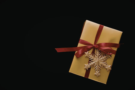 A golden gift box adorned with a red ribbon and a snowflake decoration, set against a black...