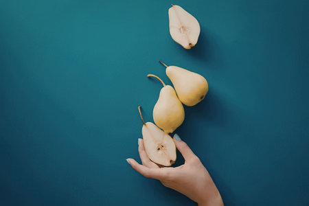 A hand holding pears against a blue background, with one pear cut in half.