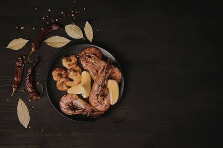 A plate of grilled shrimp and chicken garnished with lemon wedges, surrounded by spices and herbs on...
