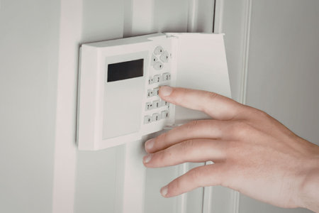 A hand pressing a button on an alarm system keypad mounted on a white wall.