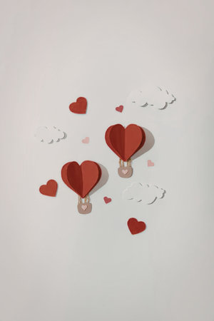 Two heart shaped hot air balloons floating in the air with clouds and hearts around them