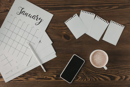 A desk setup for January with a calendar, phone, coffee, and notepads.
